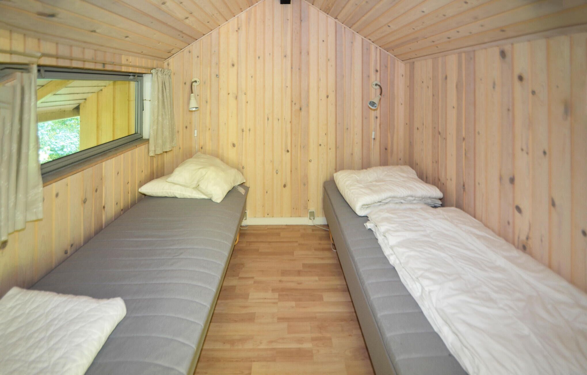 Une cabine équipée de deux lits simples, avec des murs en bois, une fenêtre et un petit luminaire.