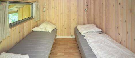 Une cabine équipée de deux lits simples, avec des murs en bois, une fenêtre et un petit luminaire.