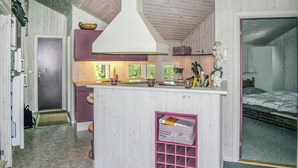 Ett kompakt kök med en central köksö, ett litet skafferi och en säng i det intilliggande rummet.