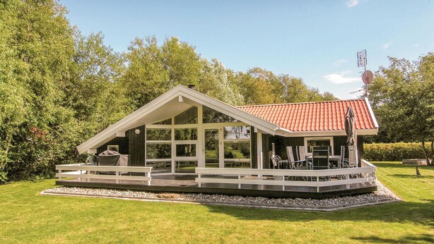 En liten, envåningsbyggnad med ett rött tegeltak, stora fönster och en täckt uteplats med utomhusmöbler.