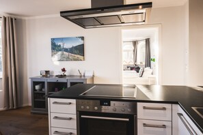 A modern kitchen with a black countertop, stainless steel appliances, and a dining area visible through an open door. - Waldfrieden - maple avenue (Altenberg)