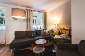 A modern living room with a sectional sofa, a round coffee table, a lamp, and a view of the outdoors through a window. - Waldfrieden - maple avenue (Altenberg)