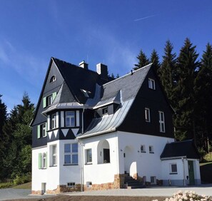 A large, two-story house with a steeply pitched roof, multiple windows, and a stone foundation. - Waldfrieden - maple avenue (Altenberg)