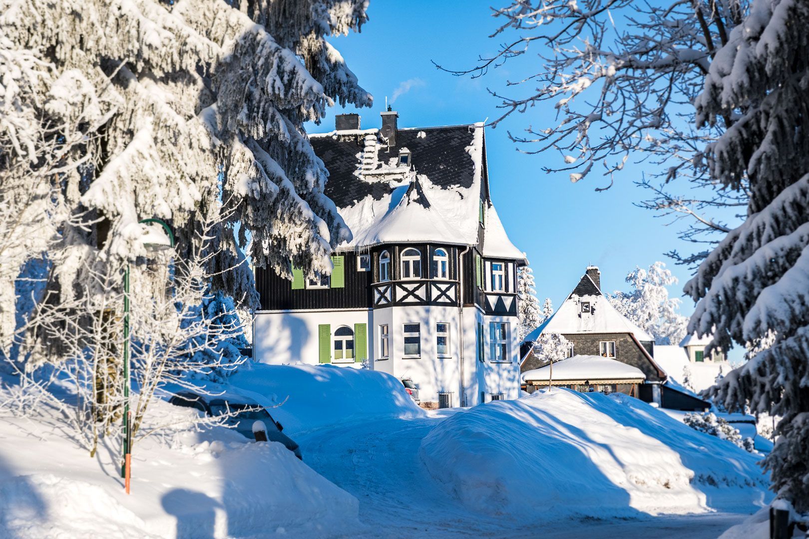 A traditional chalet-style building with a steep roof, surrounded by snow-covered trees and a clear blue sky.
