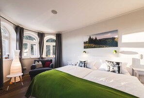 A hotel room with a bed, a chair, a lamp, a window with curtains, and a wall-mounted picture. - Waldfrieden - maple avenue (Altenberg)