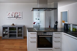 A modern kitchen with a built-in oven, a grey cabinet with glass doors, and a painting on the wall. - Waldfrieden - maple avenue (Altenberg)