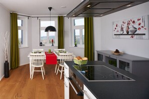 A modern kitchen with a central island, white chairs, a red table, and green curtains. - Waldfrieden - maple avenue (Altenberg)