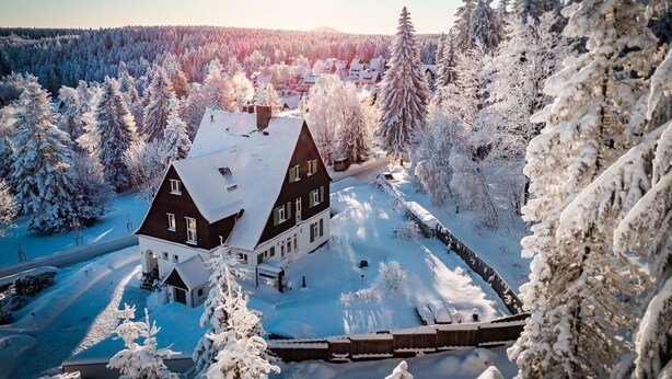 Ein großes, dunkel-gedecktes Gebäude, umgeben von schneebedeckten Bäumen und einem klaren Himmel.