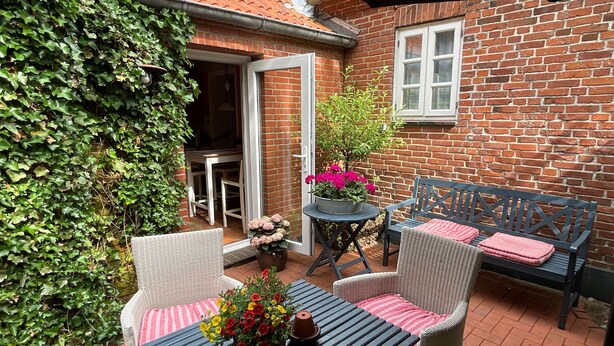 A patio with wicker furniture, a table with a candle, and potted plants.