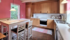 A kitchen with wooden cabinets, a white countertop, a dining table with chairs, and hanging pendant lights.