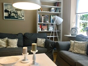 Uma sala de estar com sofá, duas velas sobre uma mesa, uma estante e um quadro na parede.