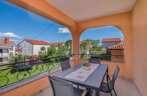 A balcony with a table and chairs, a view of neighboring houses, and a clear sky.