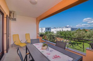 A balcony with a table, chairs, and a view of buildings and greenery.