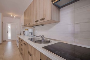 A modern kitchen with wooden cabinets, a built-in microwave, a coffee maker, a sink, and an induction cooktop.