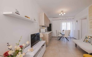 A modern apartment with a TV, dining area, and kitchenette.