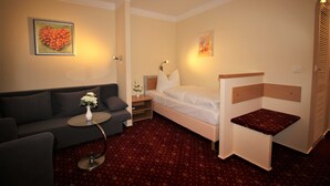 Ein Hotelzimmer mit Bett, Sofa, kleinem Tisch mit Vase und rotem Teppich.
