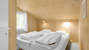 Une pièce aux murs lambrés, comprenant un lit, une fenêtre et deux lampes fixées au mur.