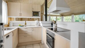 Une cuisine moderne avec des meubles en bois, un four à micro-ondes encastré, une cuisinière et une grande fenêtre donnant sur un paysage verdoyant.