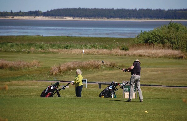 En golfbane med et vandareal i baggrunden, et flag og et skilt, der angiver 90 meters afstand.