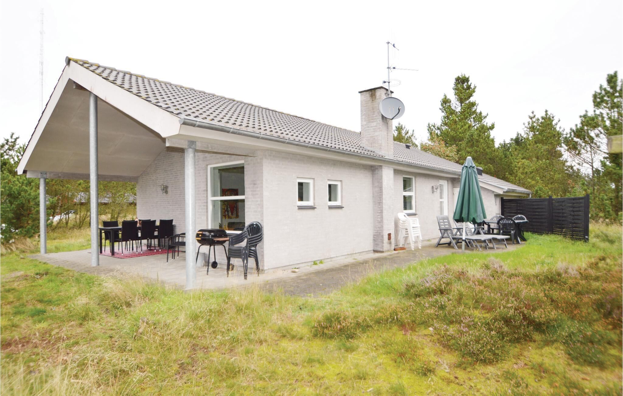 Einbungalow mit überdachter Terrasse, Satellitenschüssel und Sitzgelegenheit im Freien.