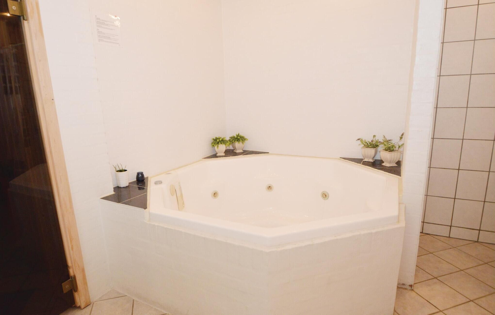 Un bagno angolare con una vasca freestanding, due piante in vaso piccole sulla parete e un pavimento piastrellato.
