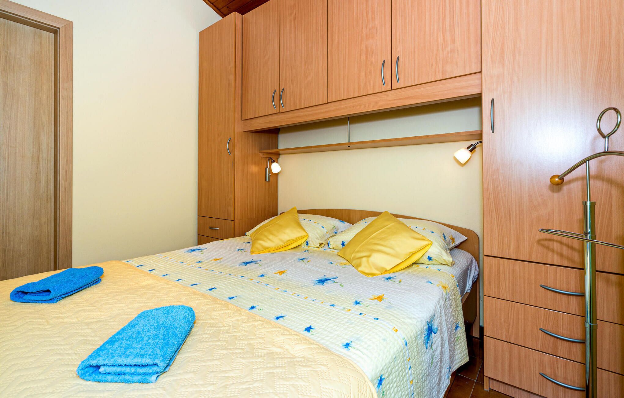 Een slaapkamer met een bed, een houten garderobe en een hanglamp.