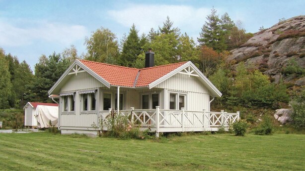 A white house with a red roof, a porch, and a white fence.