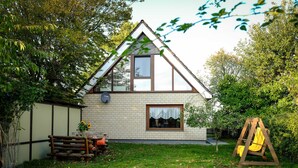 Uma casa com telhado triangular, fachada de tijolo e um balanço de madeira no quintal.