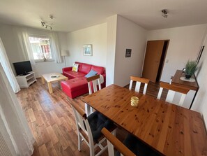 A living room with a red sofa, wooden dining table, and a TV on a stand.