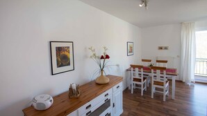 Una habitación con una mesa de comedor de madera, sillas blancas, un armario blanco y cuadros en las paredes.
