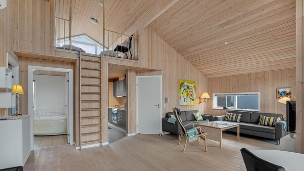 A spacious living area with a high ceiling, wooden walls, a kitchen, a dining area, and a balcony.