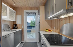 Een kleine keuken met houten wanden, roestvrijstalen apparatuur en uitzicht door een glazen deur.