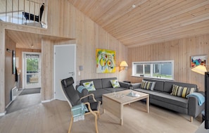 A spacious living room with a high ceiling, wooden walls, a grey sofa set, a wooden coffee table, and a black lounge chair. - Lovely home in Ulfborg with WiFi (Ulfborg)