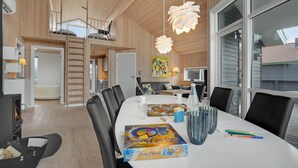 A modern kitchen with wooden cabinets, a dining table with chairs, and a loft bedroom above.