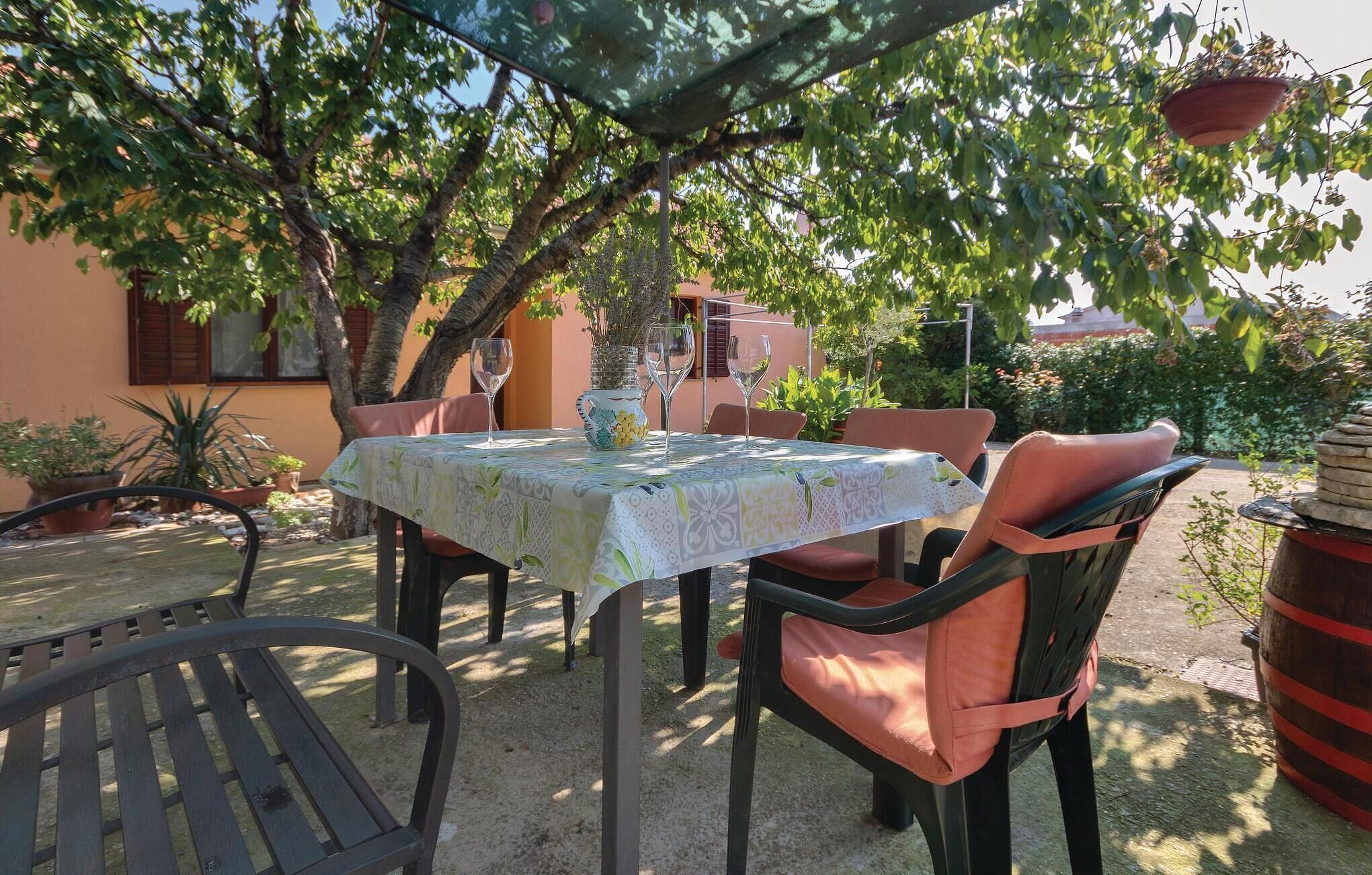 An outdoor patio with a table set for two, surrounded by chairs, under a shaded area with a pergola.