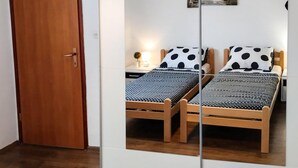 Een kamer met twee houten bedden, elk voorzien van een stippenbedovertrek en passende kussens. Er is een nachtkastje met een lamp en een kleine potplant.