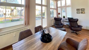A spacious room with large windows, a wooden table, and two leather chairs. - Villa Anna App. Johann Strauss - Villa Anna App. Johann Strauss (Heringsdorf)