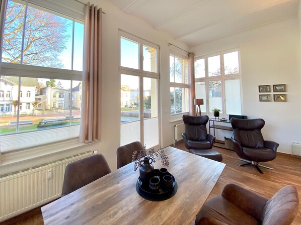 A spacious room with large windows, a wooden table, and two leather chairs.