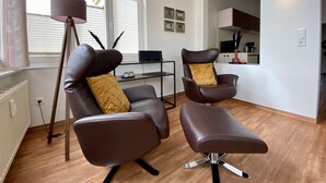 A modern living room with two leather armchairs, a small side table, and a floor lamp. There is a kitchen area visible in the background. - Villa Anna App. Johann Strauss - Villa Anna App. Johann Strauss (Heringsdorf)