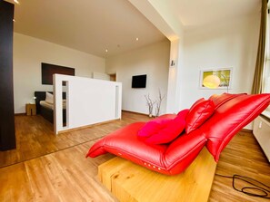 A modern living room with a red leather sofa, wooden flooring, a white partition, a flat-screen TV, and a minimalist decor.