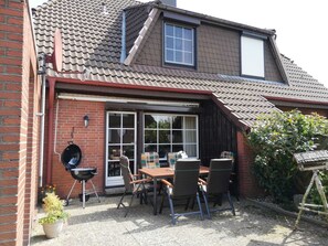 Une maison dotée d’un patio comprenant une table et des chaises, un barbecue et un pot de fleurs.