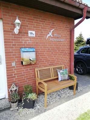 A brick building with a wooden bench, a birdhouse, and a sign that reads "Haus Mowennest."