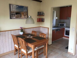 Un coin repas avec une table et des chaises en bois, une suspension décorative, une petite plante en pot et une bibliothèque remplie de livres.