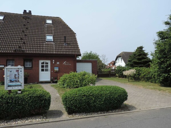 Une maison à deux étages, construite en briques, avec un toit recouvert de tuiles, une porte de garage blanche et une enseigne indiquant « Haus Mowennest ».