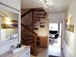 A staircase leading to a second floor, a wooden chest of drawers, a welcome sign, and a view of a beach through a window.