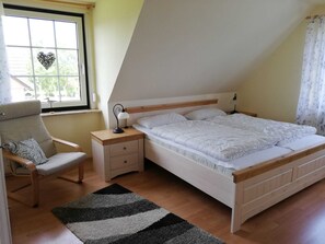 Une chambre à coucher comprenant un lit, une chaise, une table de chevet, une lampe et une fenêtre décorée d’un motif en forme de cœur.