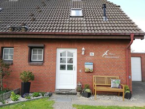 A red brick house with a white door, a bench, and potted plants.