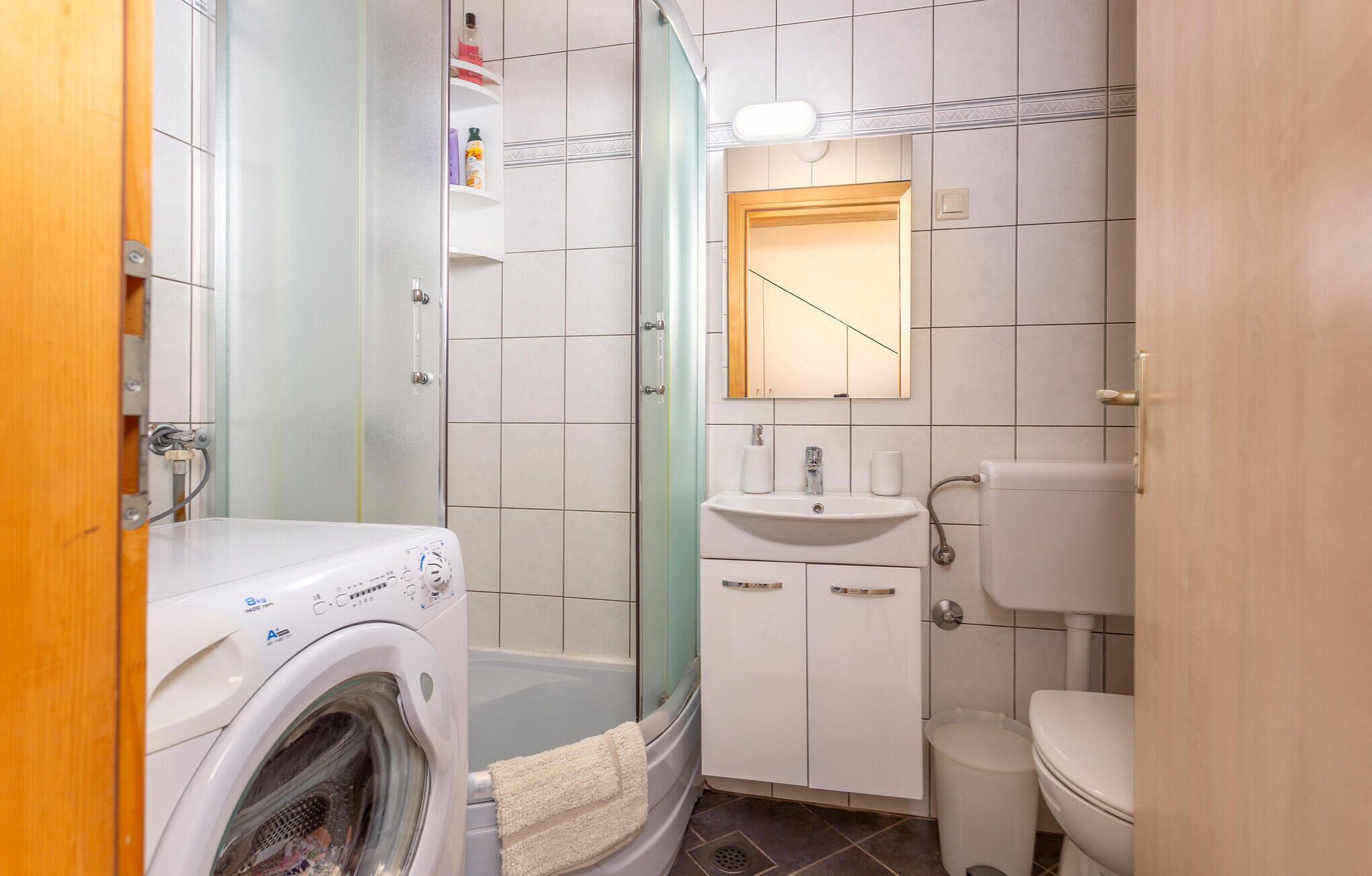 A compact bathroom with a washing machine, a sink, a toilet, and a shower enclosure.