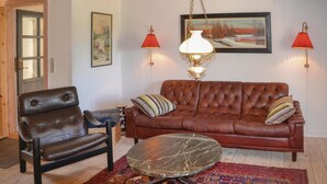 Een woonkamer met een bruine leren bank, een bijpassende leren fauteuil, een marmeren salontafel en twee rode wandlampen.