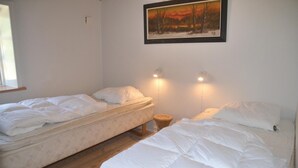 Een slaapkamer met twee eenpersoonsbedden, een houten vloer, een aan de muur hangend schilderij en twee bedlampjes.